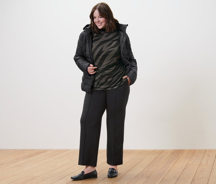 Femme posant en veste matelassée à capuche, haut manches longues à col roulé en mesh imprimé et pantalon en jersey avec passepoil.