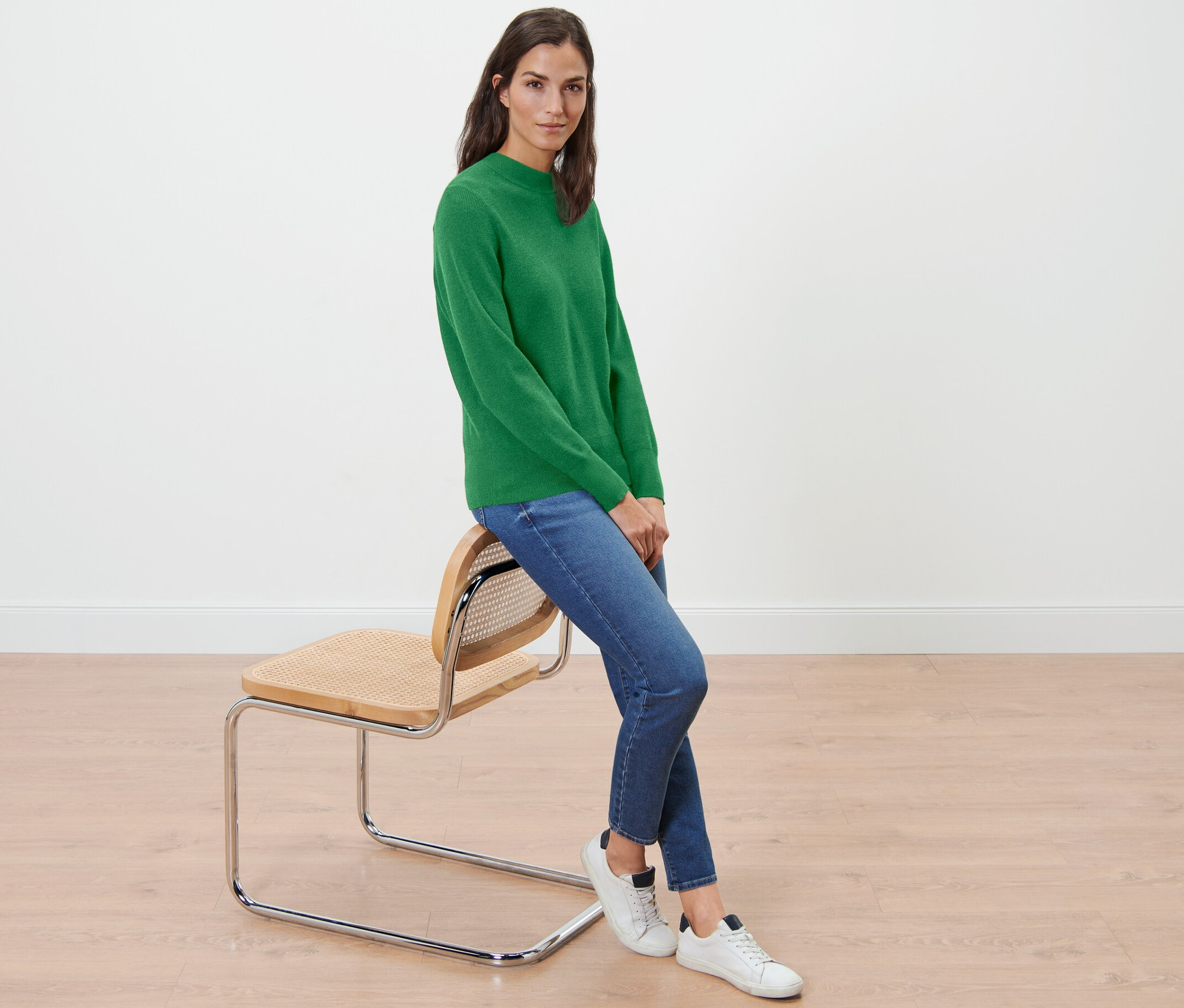 Une femme est assise sur une chaise et porte un pull vert en maille fine.