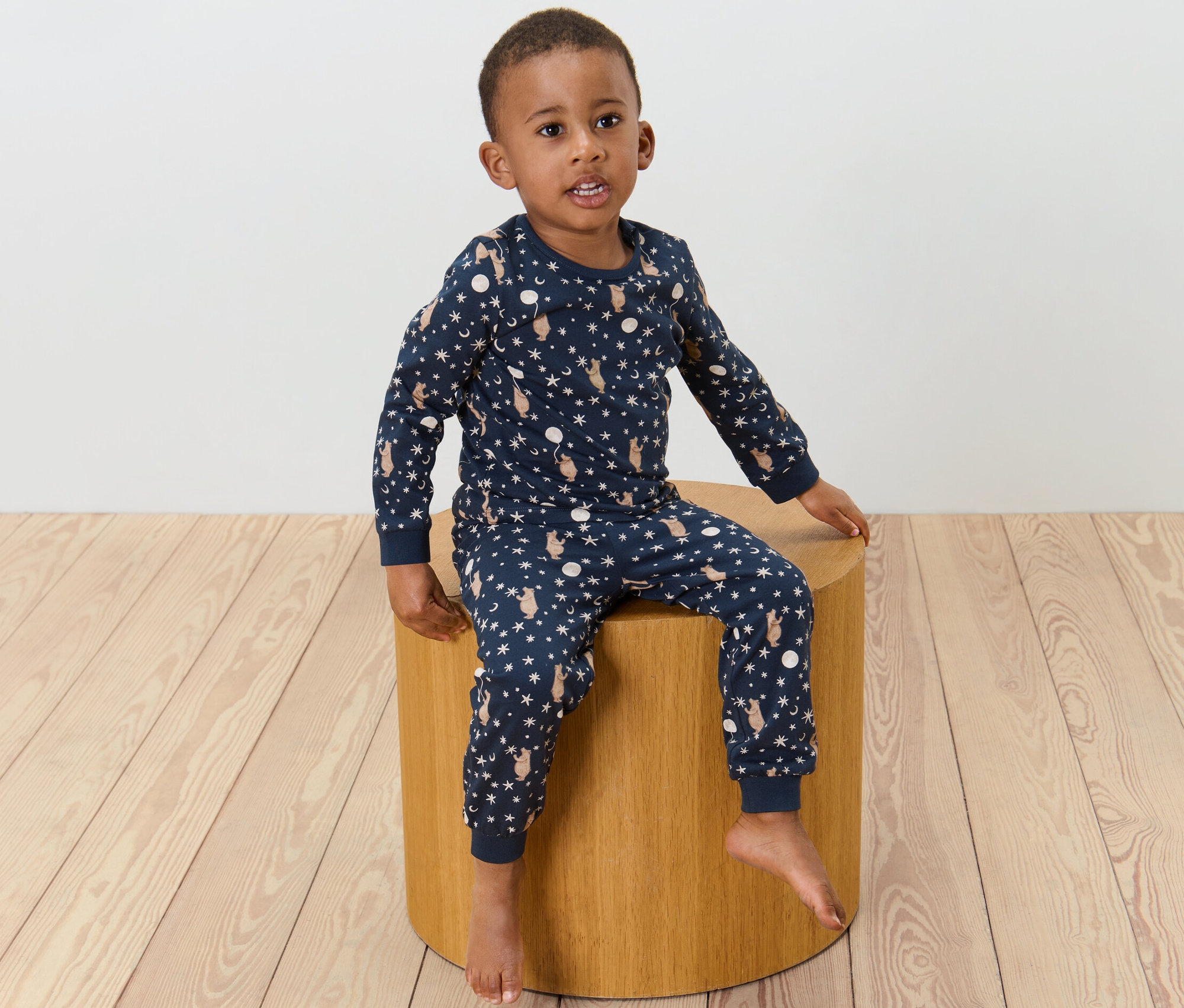Un garçon est assis sur un tabouret et porte un pyjama pour enfant imprimé.