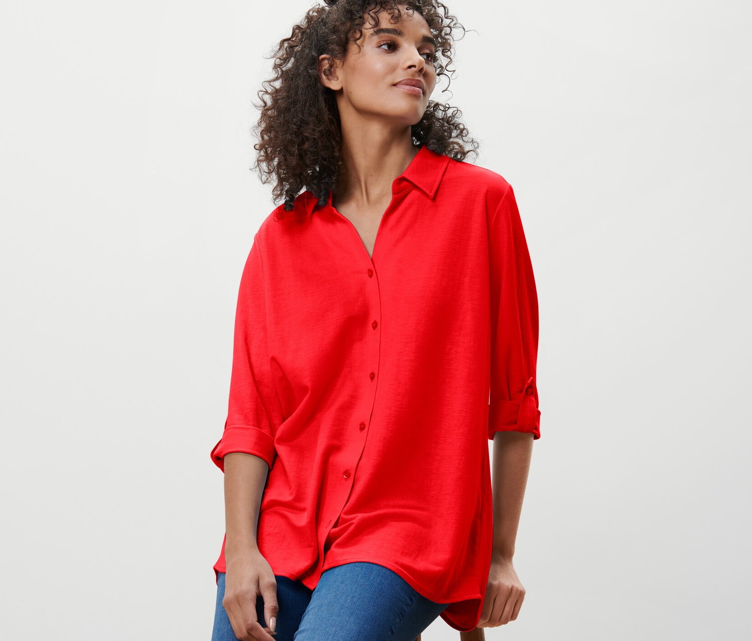 Une femme est assise sur un tabouret et porte un chemisier rouge en jersey piqué.
