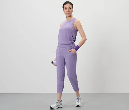 Une femme debout tenant une bouteille d'eau violette. Elle porte un haut violet et un pantalon de sport 3/4.