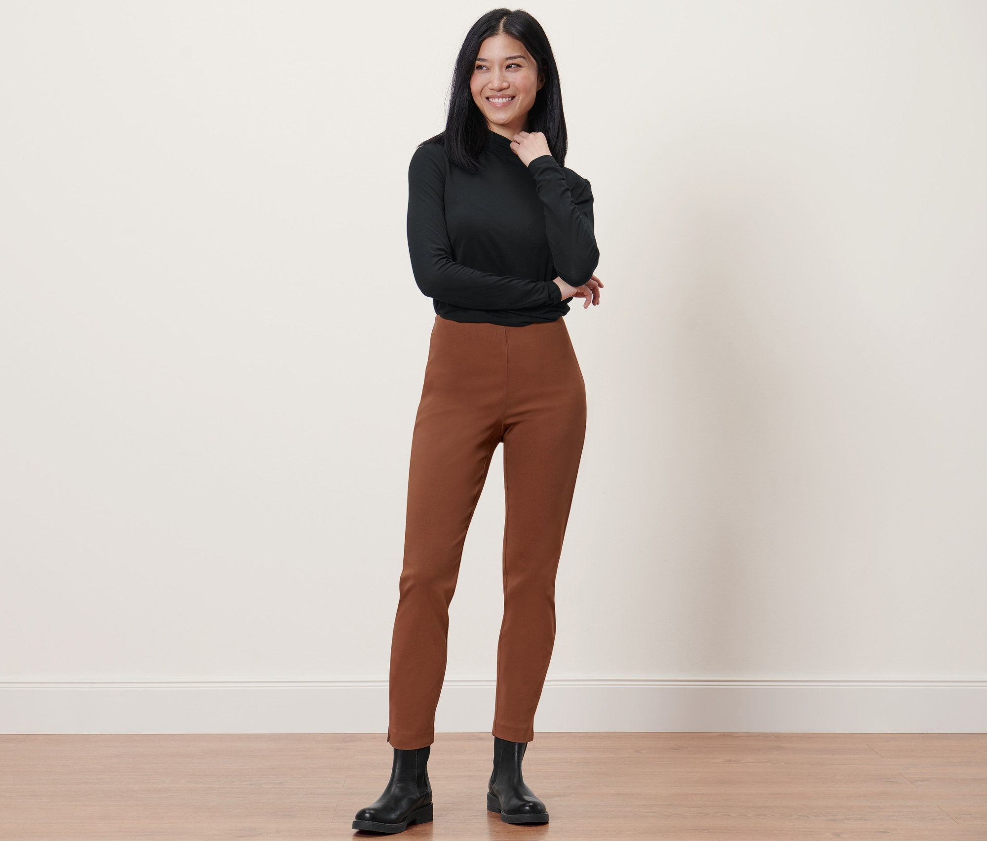 Femme posant dans un haut noir et un pantalon stretch cognac.