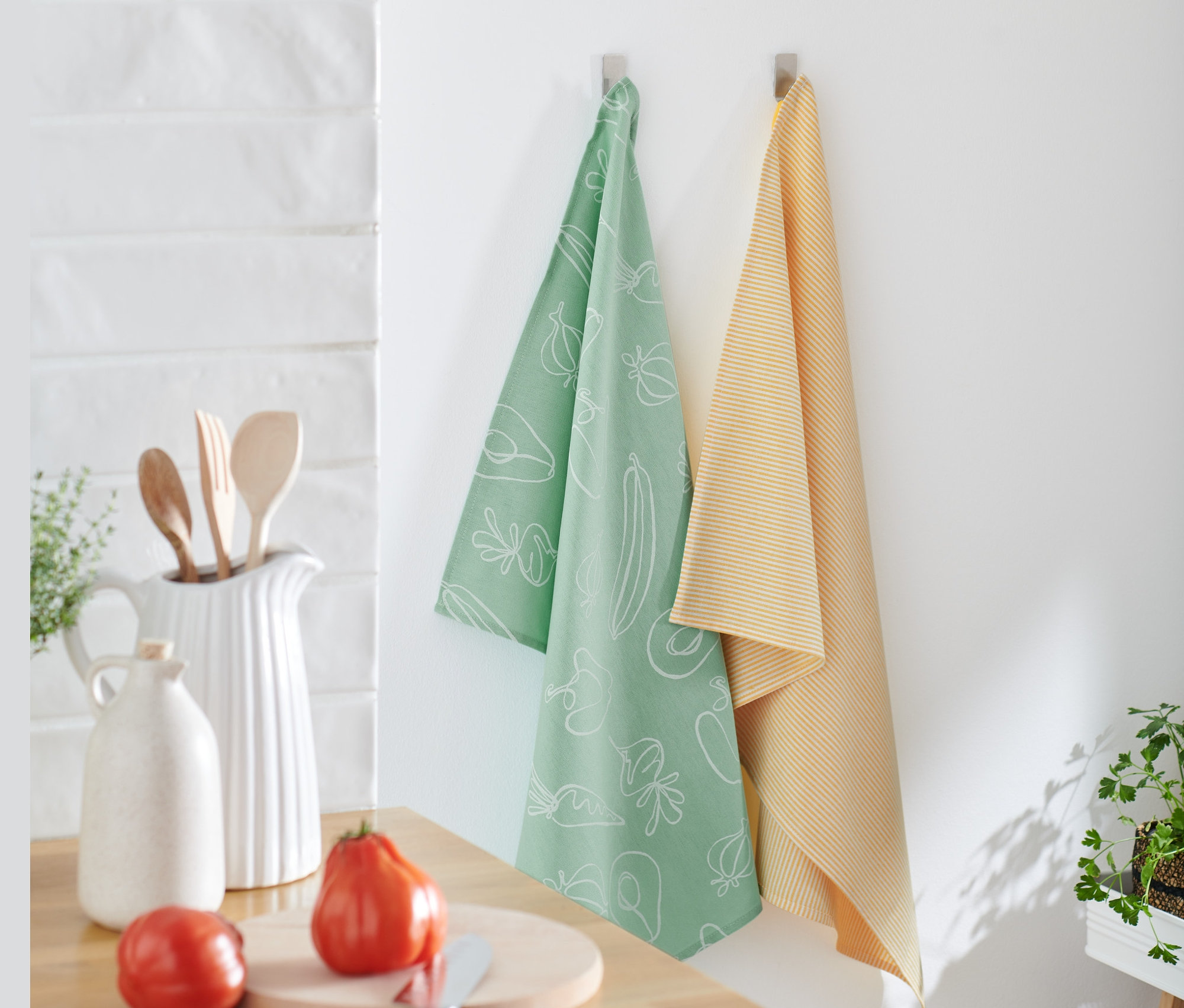 Deux linges de cuisine sont accrochés au mur, un vert clair avec un imprimé de légumes blancs et l'autre jaune rayé. 2 linges de cuisine