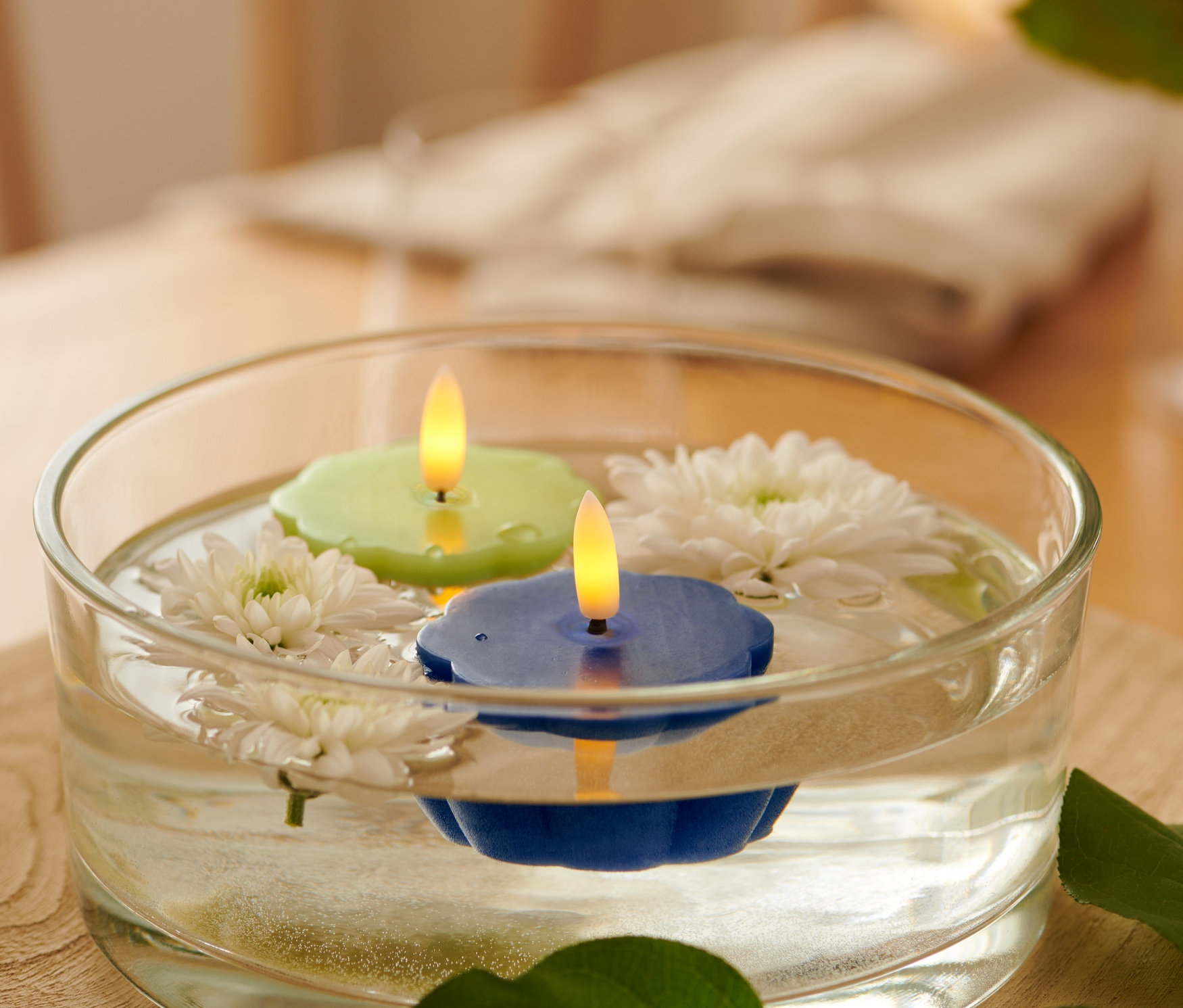 Dans un bol en verre, deux bougies chauffe-plat flottantes en cire véritable avec LED, une verte et une bleue, et des fleurs blanches.