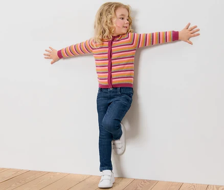 Une fille appuyée contre un mur blanc porte un jean pour enfant – Fit « Lotta ».