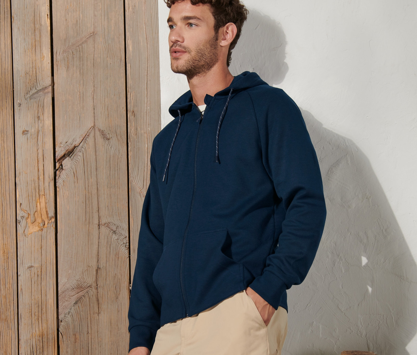 Un homme pose en jaquette sweat fonctionnelle bleu marine et pantalon beige.