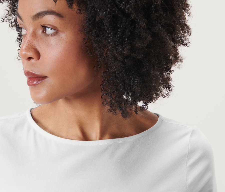 Portrait d'une femme aux cheveux bruns et bouclés portant un t-shirt blanc à manches trois-quarts.