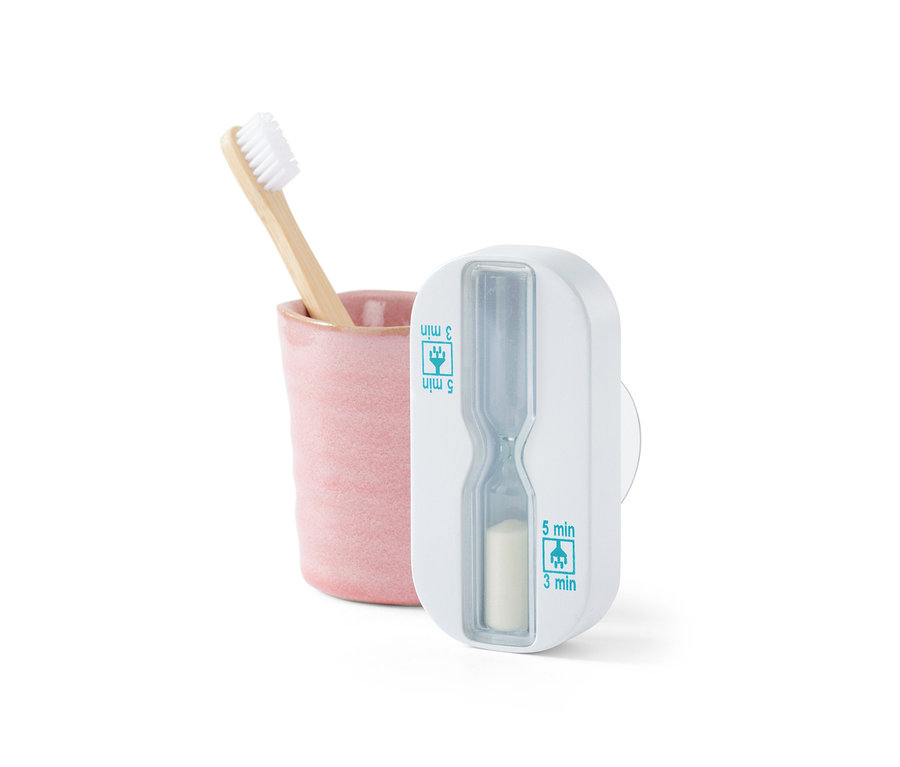Brosse à dents en bambou dans un gobelet rose à côté d'un sablier de douche blanc.