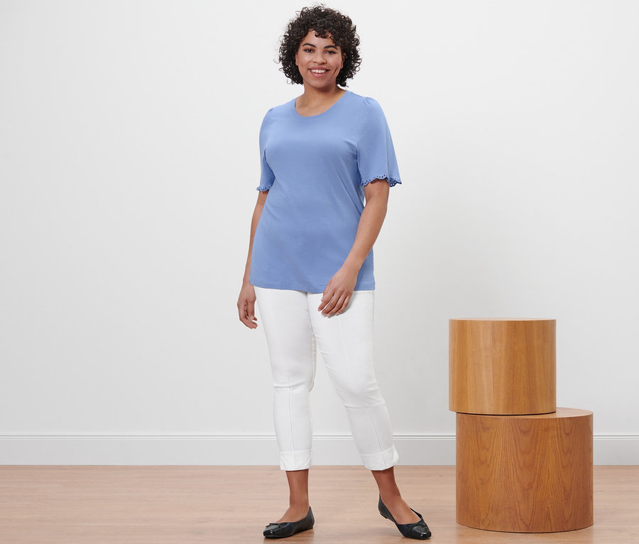 Femme posant en chemise bleu clair avec des fronces et un pantalon stretch blanc.