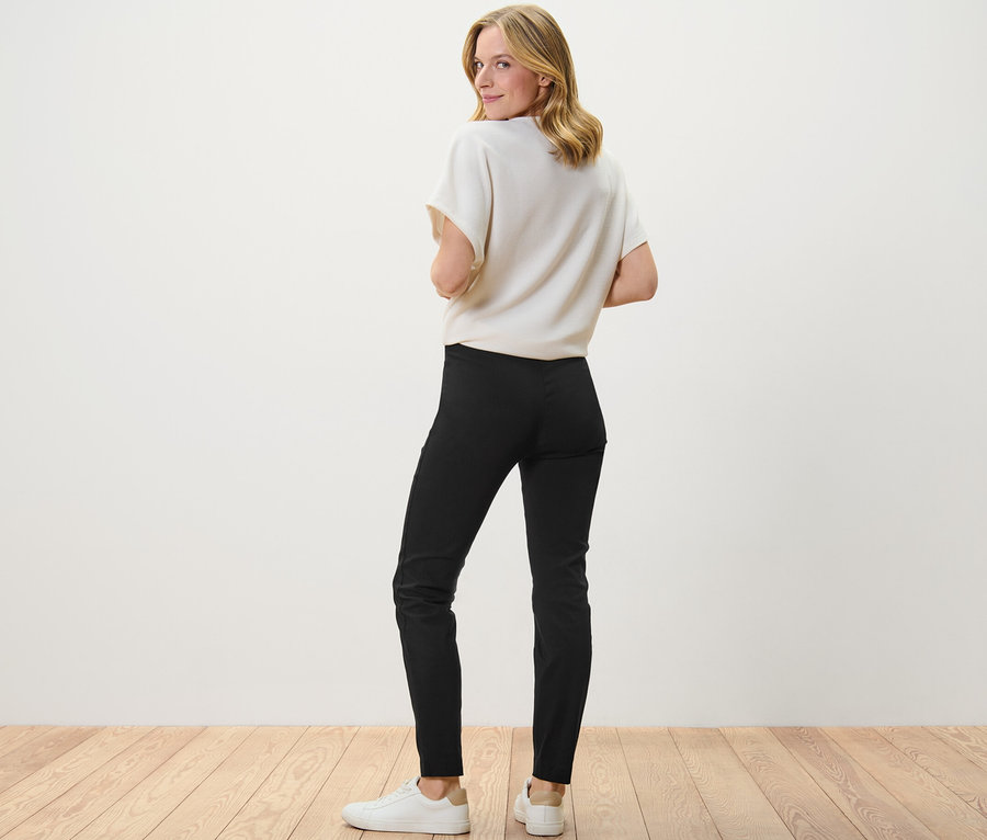 Une femme regarde par-dessus son épaule et porte un pantalon stretch noir.