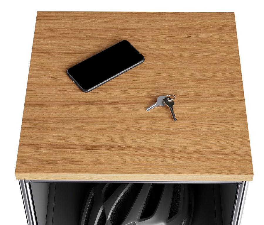 Sur le plateau en bois de la commode étroite en métal « CN3 », il y a un téléphone portable et des clés. Un casque de vélo est visible dans le compartiment rabattable ouvert.