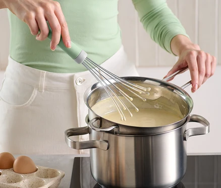 Une femme mélange de la crème dans une casserole avec un fouet peu encombrant.