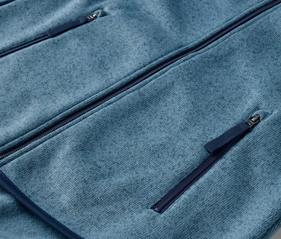 Gros plan sur une veste en polaire tricotée bleu foncé avec des poches zippées.