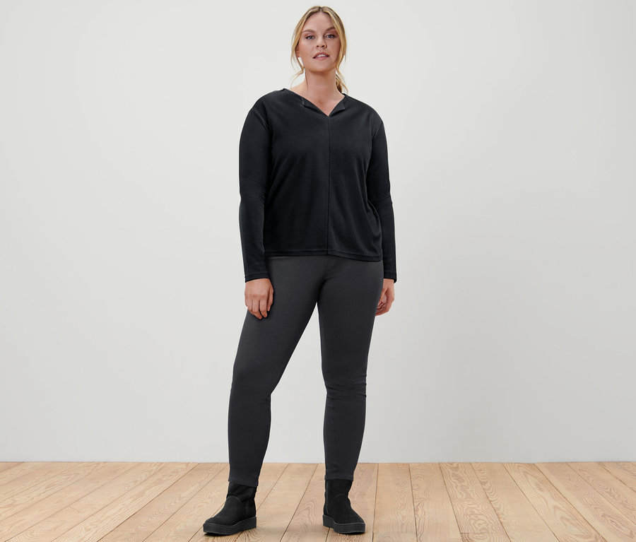 Femme debout portant une blouse noire et un jegging.