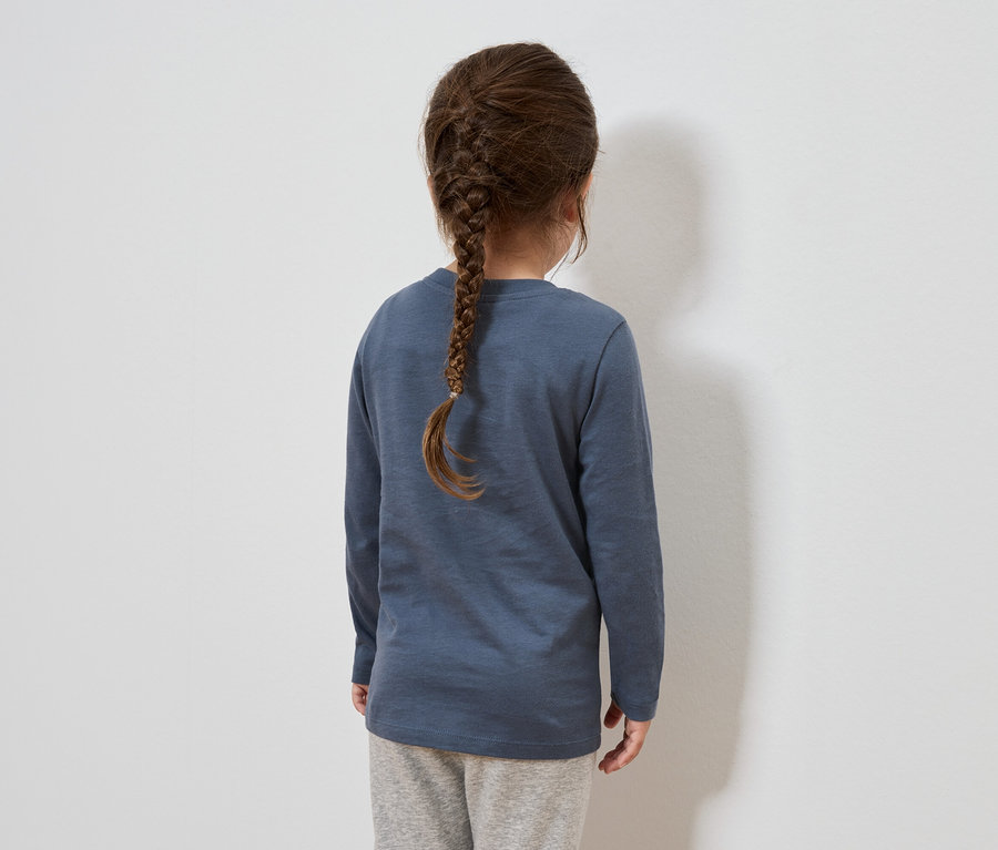 Vue de dos, une fille aux cheveux bruns tressés en une natte. Elle porte un t-shirt bleu à manches longues et un pantalon de survêtement gris.