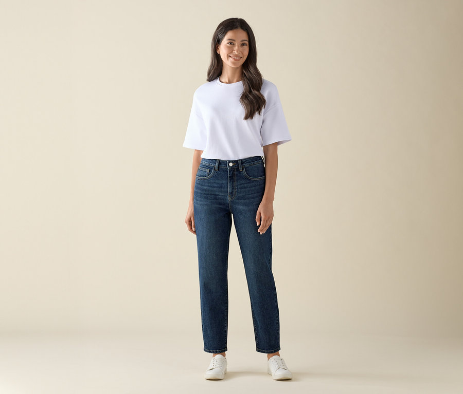 Une femme porte un Mom Jeans – Coupe « Nyla », bleu foncé et un t-shirt blanc.