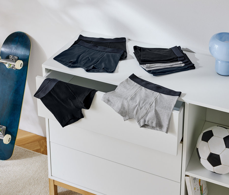 Des boxers pour hommes sont posés sur une commode, à côté d'un skateboard et d'un ballon de football.