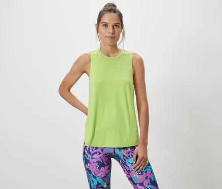 Femme posant dans un débardeur de sport vert citron d'un ensemble deux pièces et un legging à motifs.