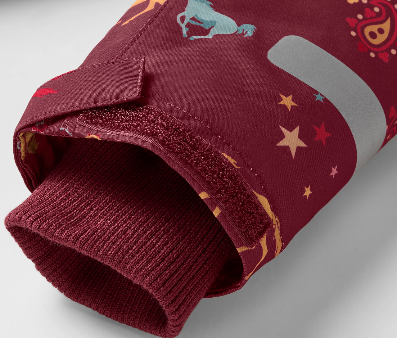 Détail d'une manche de veste bordeaux avec des motifs de chevaux et d'étoiles, finie par un bord bordeaux.