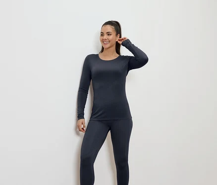 Une femme souriante en sous-vêtements thermiques bleu foncé pose sur un fond blanc.