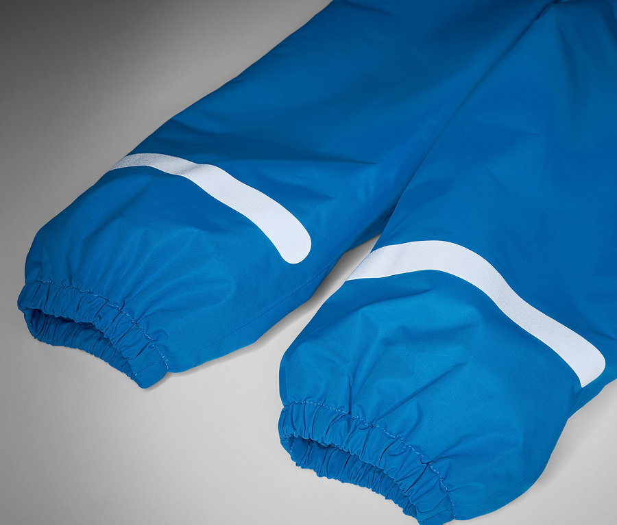 Gros plan sur un pantalon de pluie thermique bleu pour enfant avec des bandes réfléchissantes blanches.