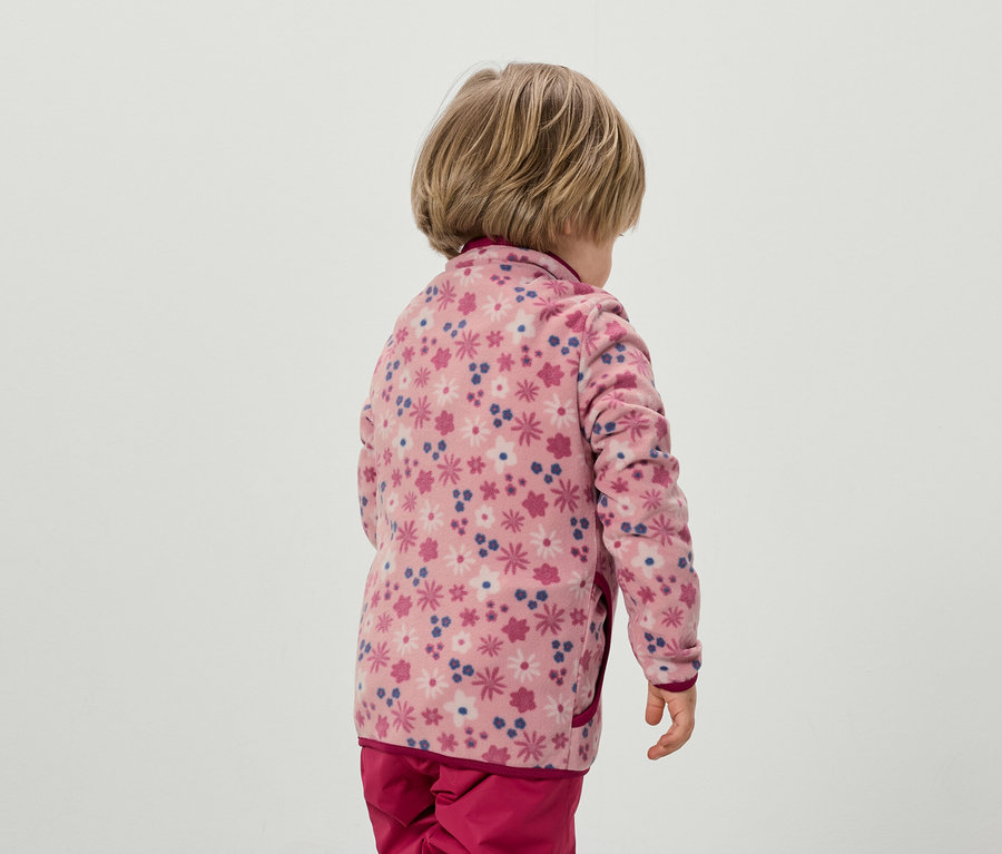 Enfant de dos, portant une veste en polaire rose à motif floral et un pantalon rose.