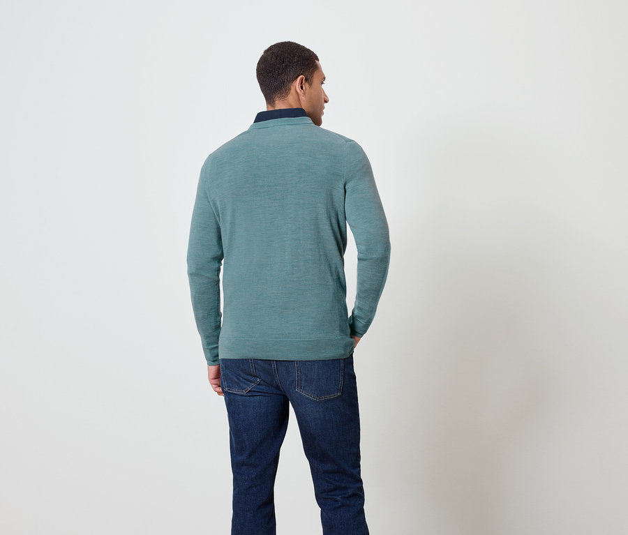 Un homme vu de dos porte un pull bleu-vert et un jean.
