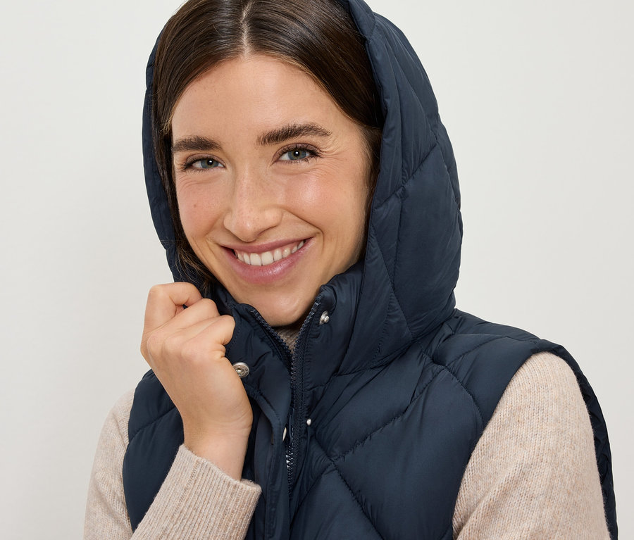 Femme souriante portant une doudoune sans manches bleu marine à capuche.