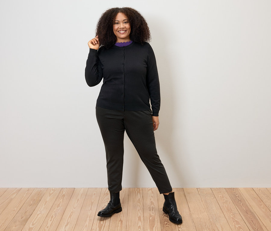 Femme posant en cardigan en maille fine noir, pantalon et bottes.