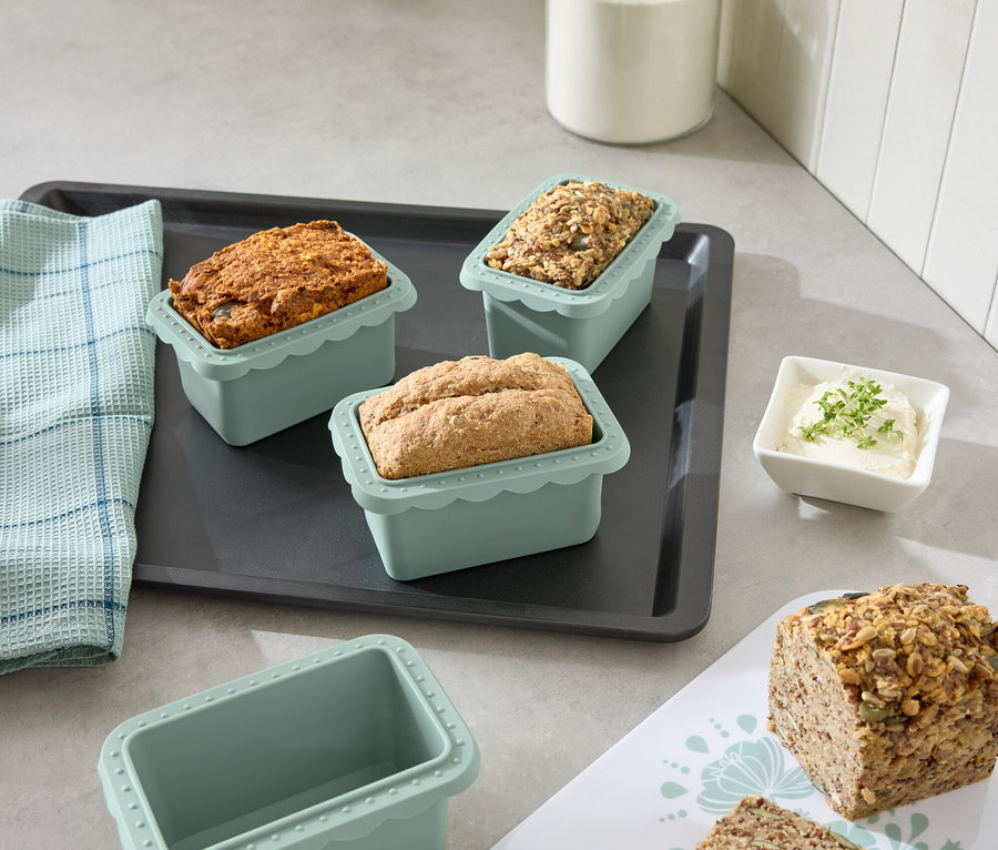 Sur une table de cuisine, des mini-moules à pâtisserie contenant différents types de pain sont disposés sur une plaque de cuisson.