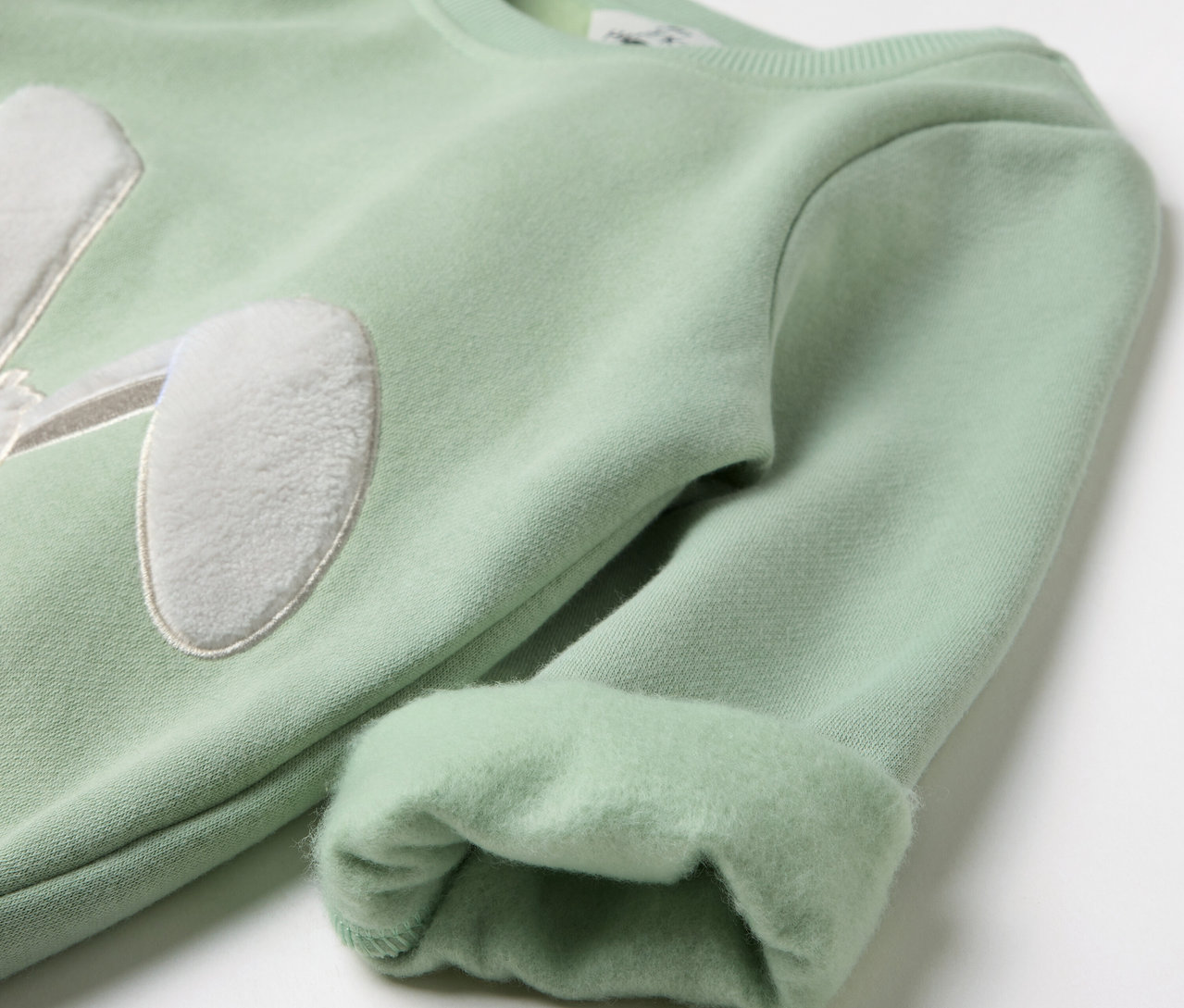 Pull vert clair avec application oreilles de lapin sur la poitrine et manches retroussées.