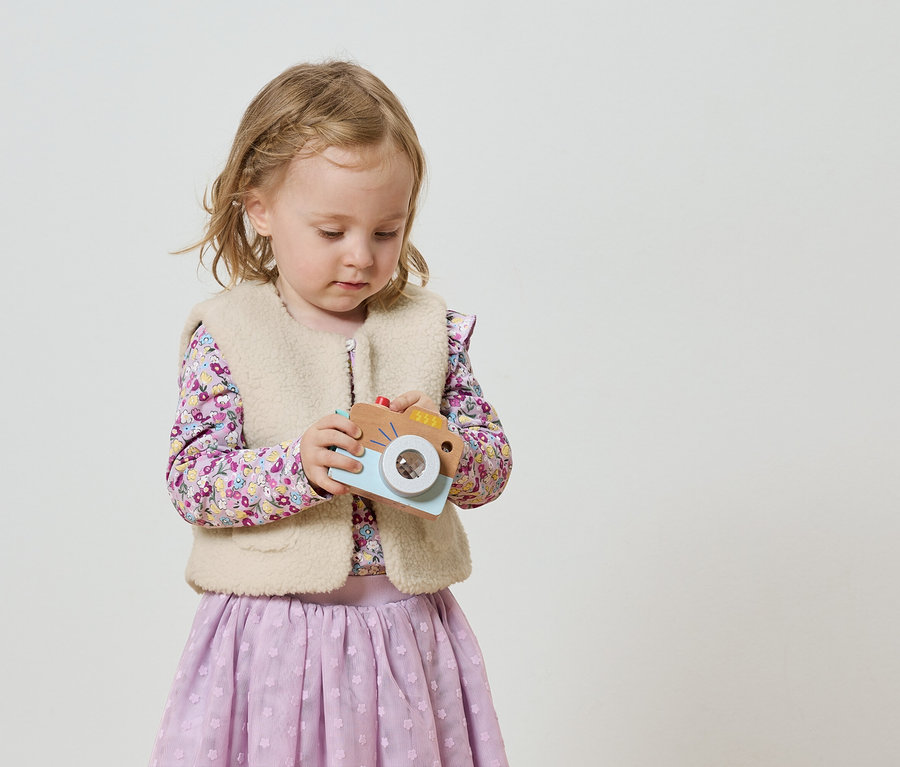 Une petite fille avec des tresses blondes tient un appareil photo jouet.