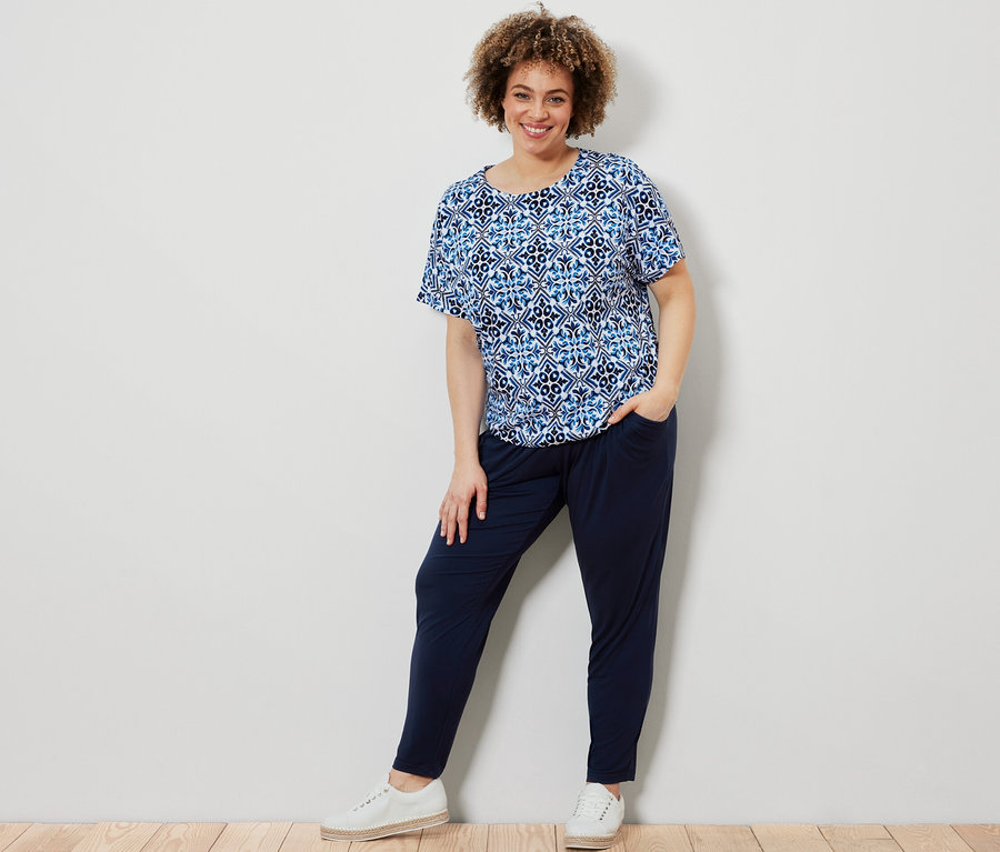 Femme posant en blouse imprimée bleue et pantalon en jersey bleu foncé.