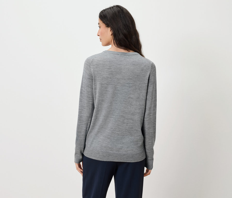 Vue de dos, une femme aux longs cheveux bruns porte un pull gris et un pantalon bleu marine.