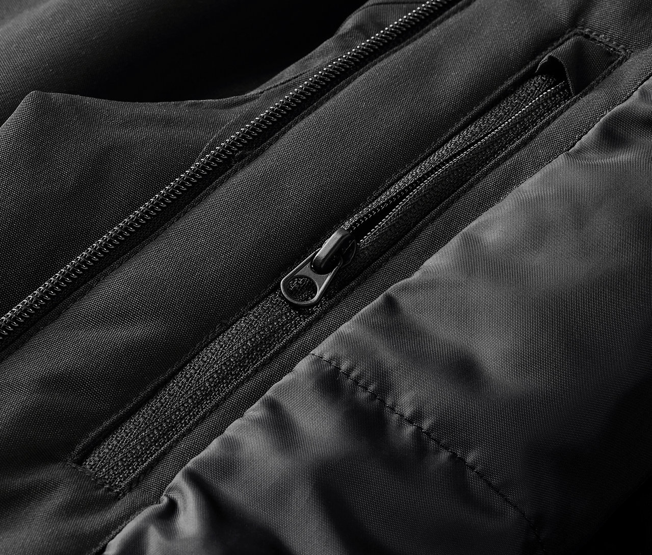 Gros plan sur une veste noire avec des fermetures éclair apparentes et des coutures matelassées.