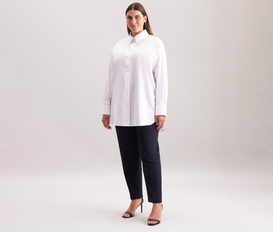 Femme portant une blouse-chemise blanche Seidensticker grande taille, un pantalon foncé et des sandales noires.