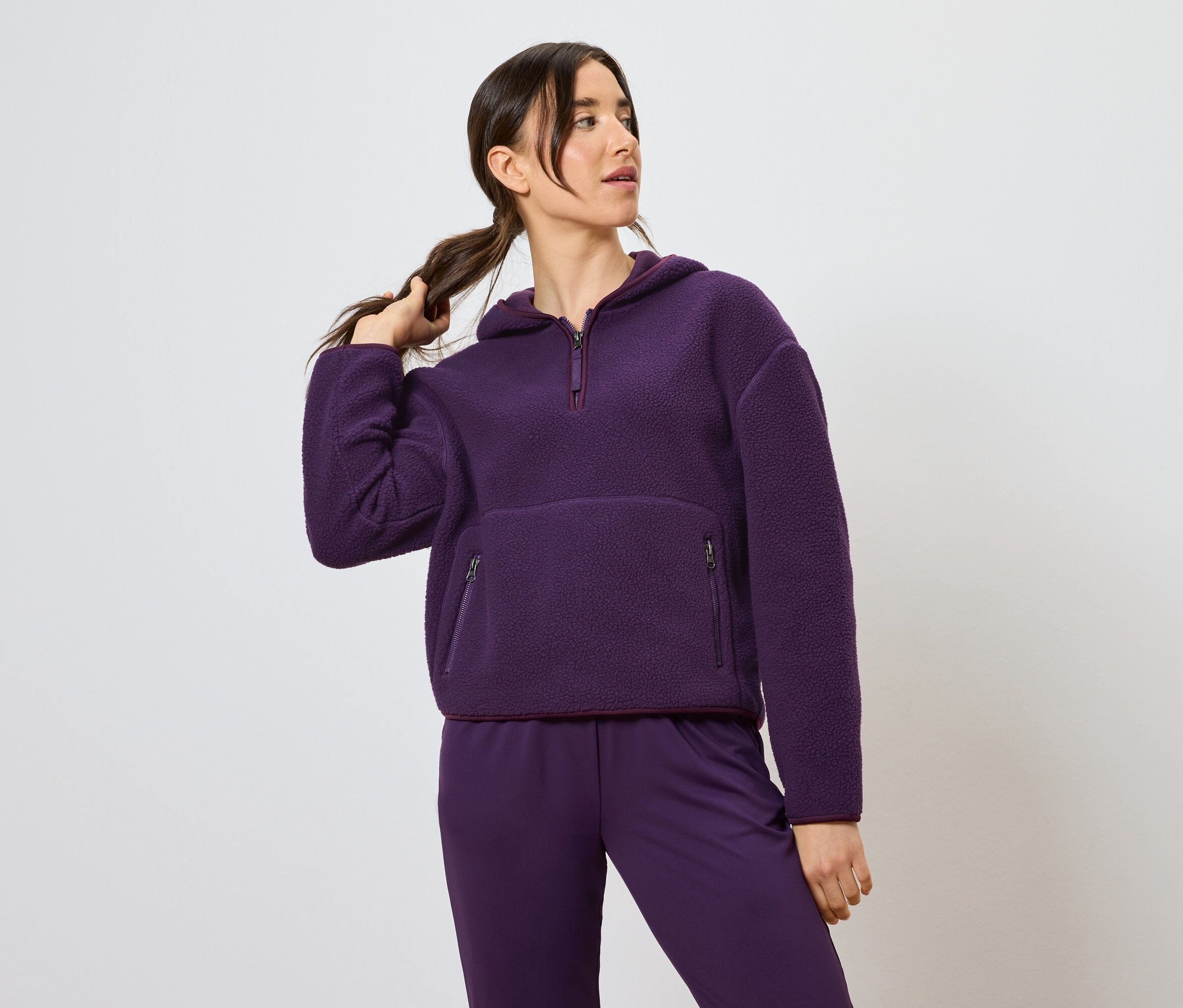Femme tenant une queue de cheval, portant un sweat à capuche violet et un pantalon.