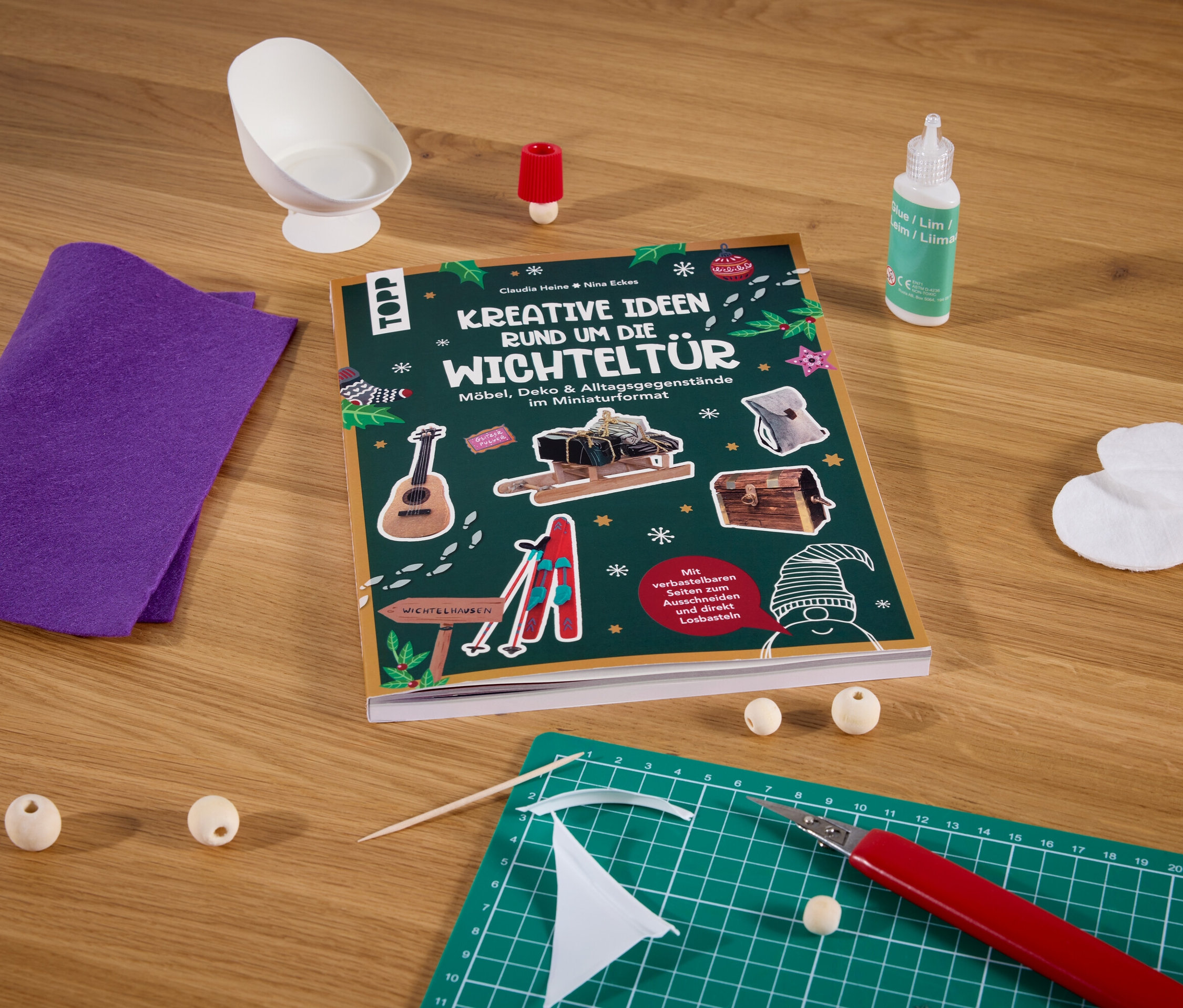 Le livre »Kreative Ideen rund um die Wichteltür« est posé sur une table avec d'autres fournitures de bricolage.