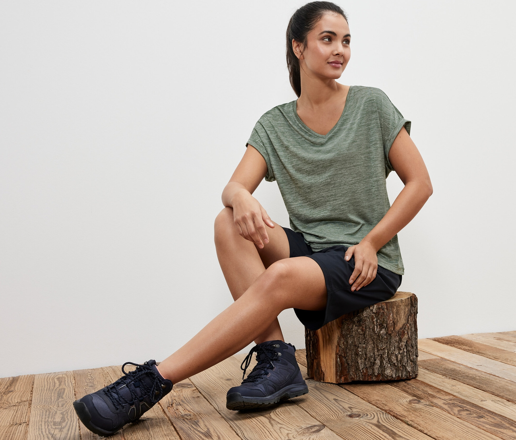 Femme assise sur un billot de bois portant un t-shirt fonctionnel kaki.