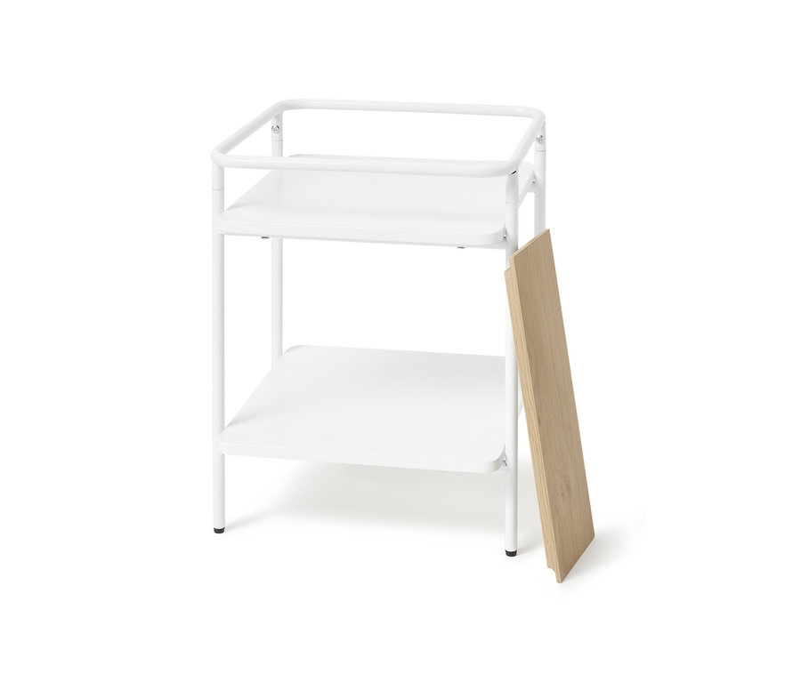 Table d’appoint blanche avec deux étagères et un panneau en bois appuyé sur le côté.