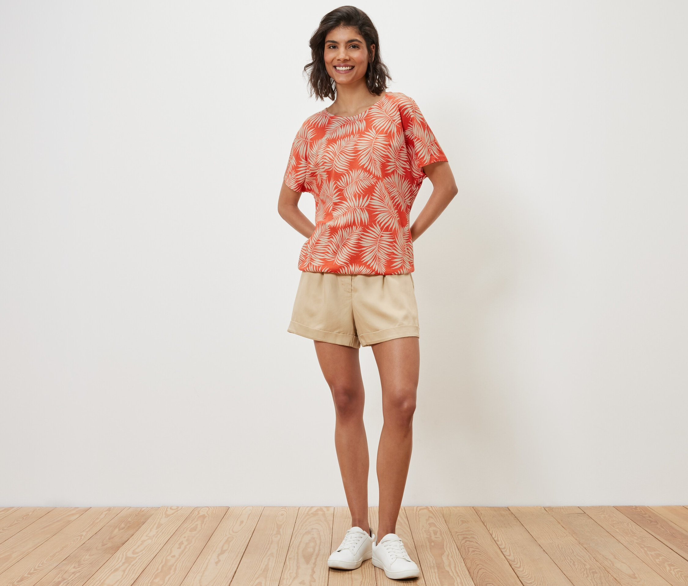 Une femme pose, portant une blouse imprimée, un short et des baskets.