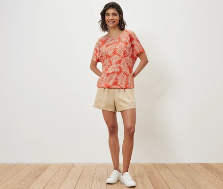 Une femme pose, portant une blouse imprimée, un short et des baskets.
