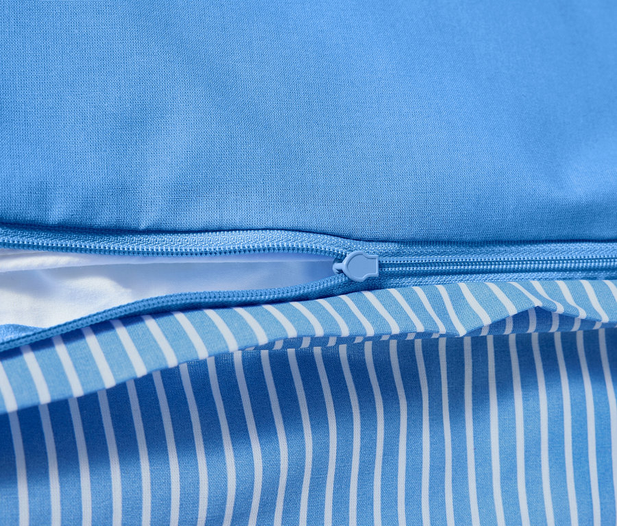 Gros plan d'une parure de lit en renforcé avec fermeture éclair et motif rayé bleu et blanc.