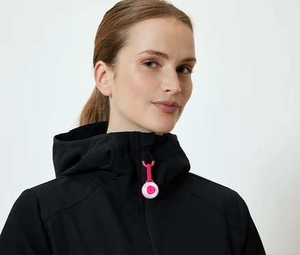 Une femme porte une veste noire à capuche avec une fermeture éclair rose.