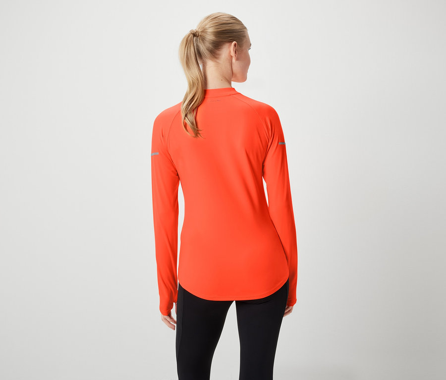 Vue arrière d'une femme aux cheveux blonds attachés en queue de cheval, portant un haut de sport orange à manches longues et un legging noir.