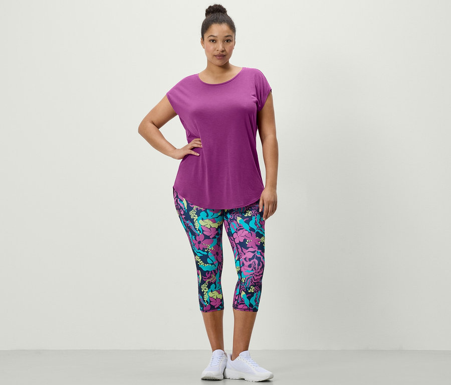 Femme posant dans un T-shirt de sport violet et un collant de sport 3/4 avec imprimé intégral.