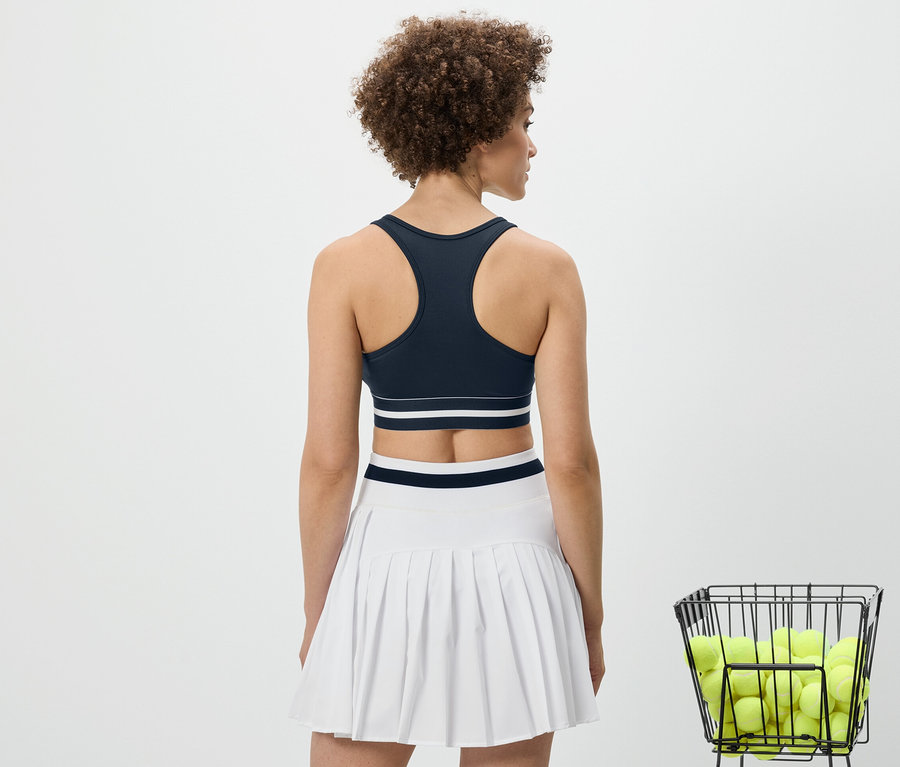 Vue arrière d'une femme portant un bustier de sport « Crop Top » bleu et une jupe blanche.