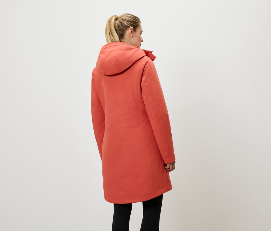 Une femme vue de dos porte un manteau corail à capuche et un legging noir.