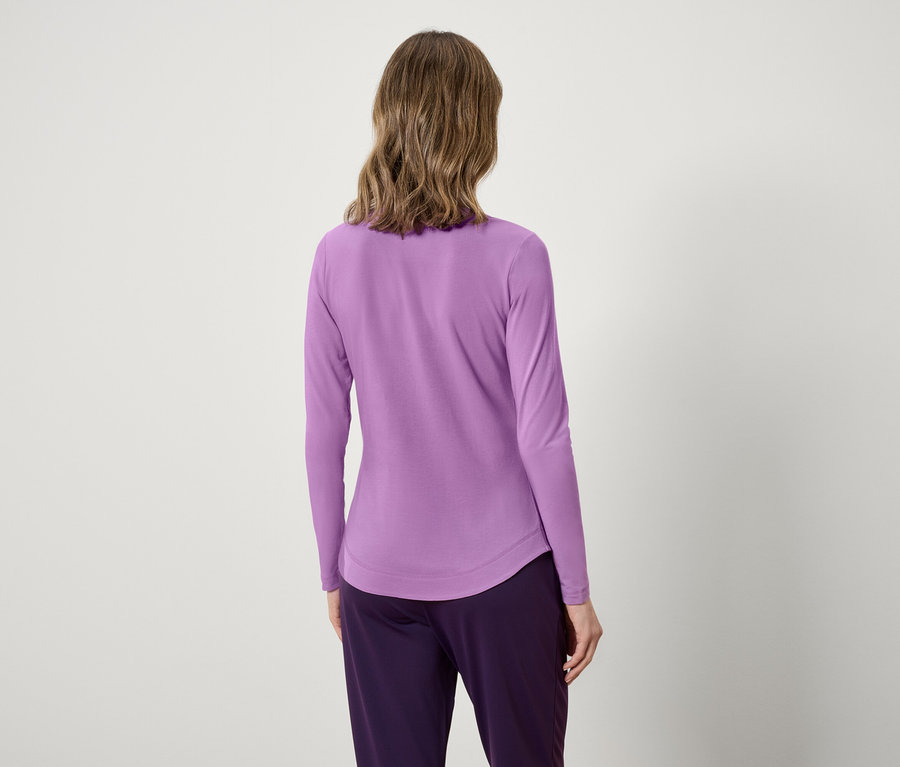 Vue arrière d'une femme aux cheveux ondulés portant un haut à manches longues lavande et un pantalon violet.