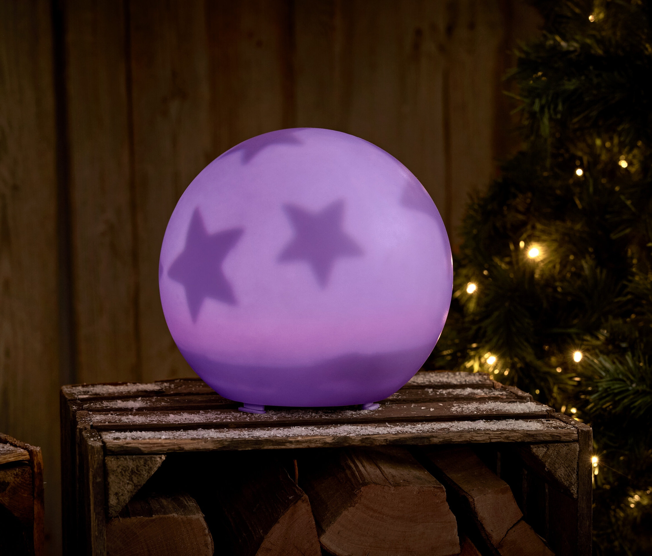 Boule violette avec des étoiles sur une caisse en bois à côté d'un arbre de Noël.